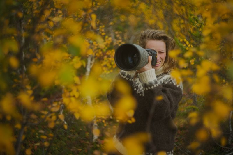 Caucasian female photographer taking picturesof wildlife with camera and telephoto lens in a beautiful yellow autumn forest, adult woman with camera